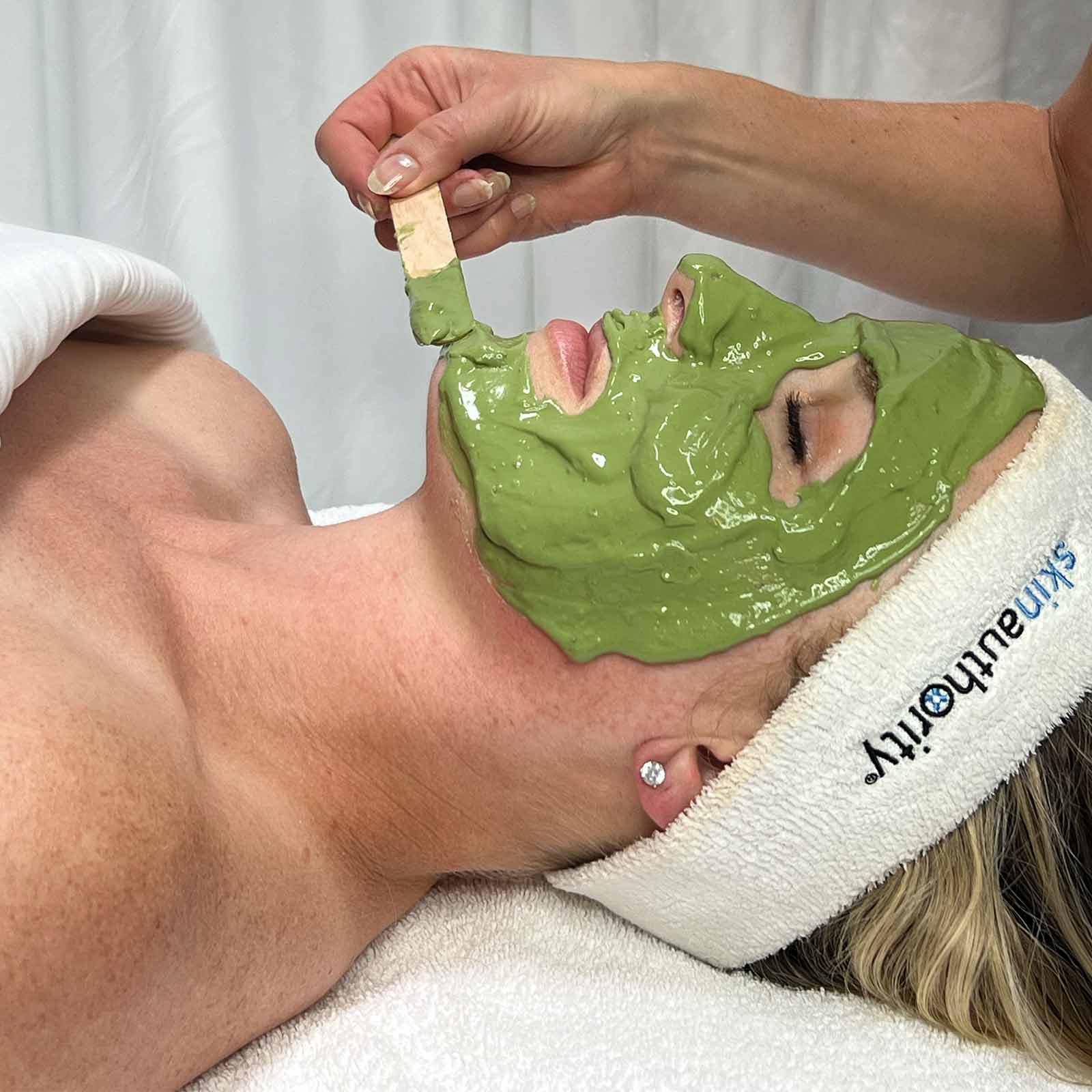 Person receiving a green facial mask treatment with a towel labeled 'Sculpture' on a neutral background.