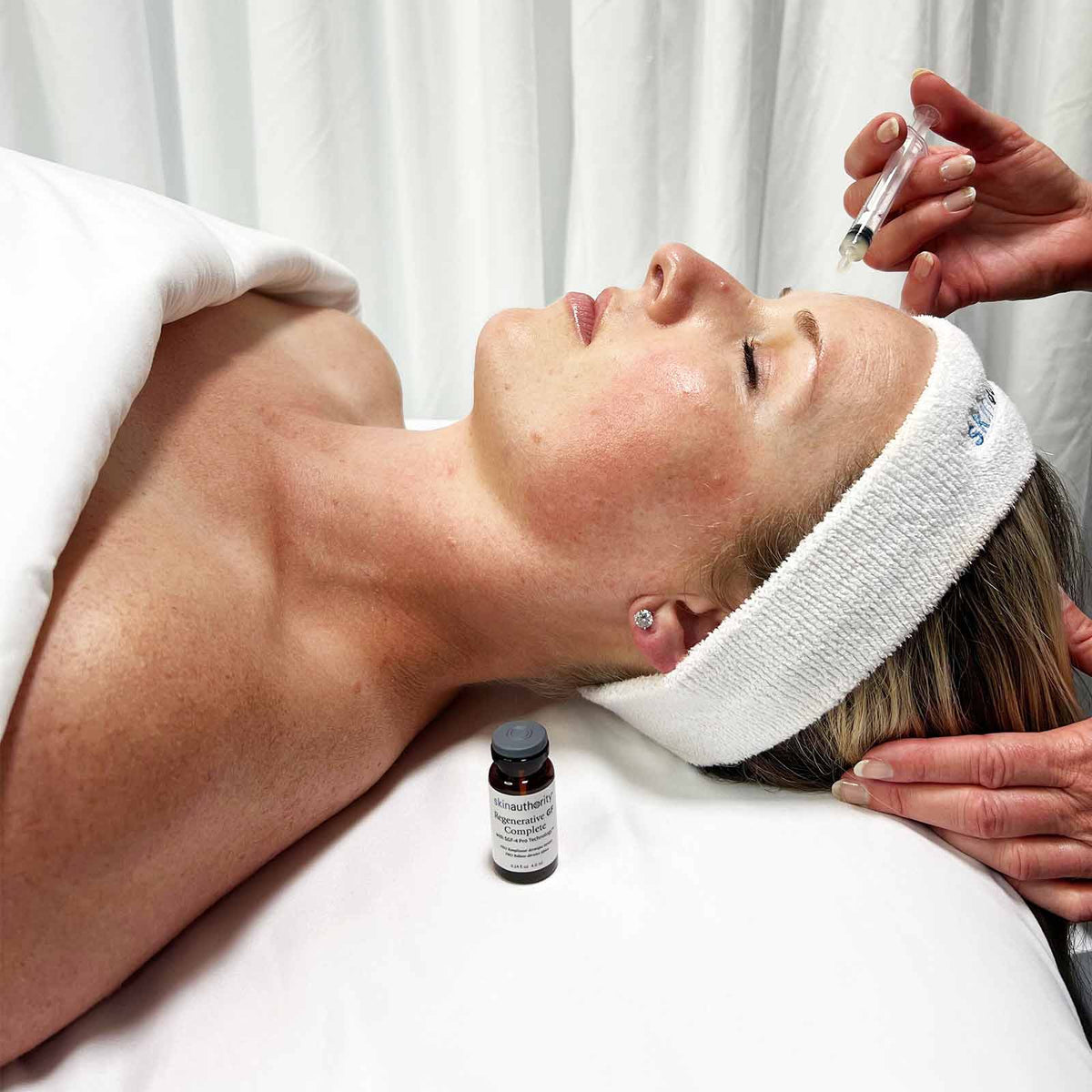 Woman receiving a facial treatment with a skincare product on a white background