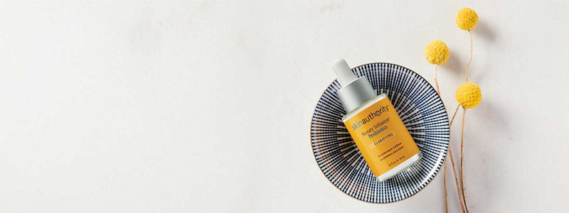 Skincare serum bottle on a decorative plate with yellow flowers on a light background
